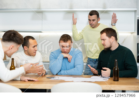 Brainstorming - male friends drinking beer and trying to solve financial problems by consulting each other while sitting at table Brainstorming - male friends drinking beer and trying to solve financial problems by consulting each other while sitting at table 129457966
