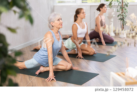 Womens different ages practicing yoga lesson at sport club Womens different ages practicing yoga lesson at sport club 129458072