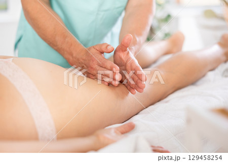 Woman covered with white towel lies and enjoys during anti-cellulite massage in hips and legs Woman covered with white towel lies and enjoys during anti-cellulite massage in hips and legs 129458254
