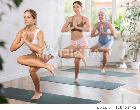 Fitness, sport and healthy lifestyle concept: woman different ages doing yoga pose - vrikshasana pose on mat in studio Fitness, sport and healthy lifestyle concept: woman different ages doing yoga pose - vrikshasana pose on mat in studio 129458442