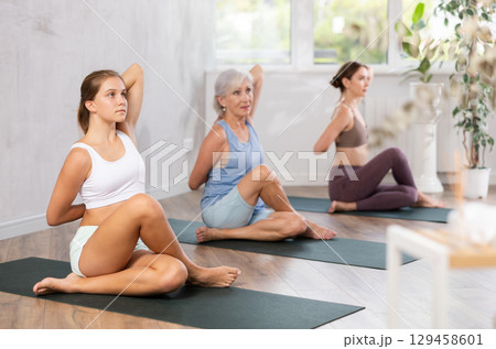 Three generations of women perform sitting Gomukhasana cows head in gym Three generations of women perform sitting Gomukhasana cows head in gym 129458601