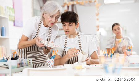 Elderly woman assisting adult son painting ceramic mugs in family workshop Elderly woman assisting adult son painting ceramic mugs in family workshop 129458604