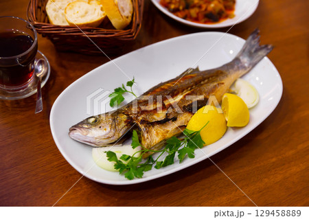 Delicious fish dish, fried bass served with onion, lemon and parsley 129458889