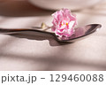 A close-up photograph of a small, delicate pink flower resting on a shiny, silver spoon. 129460088