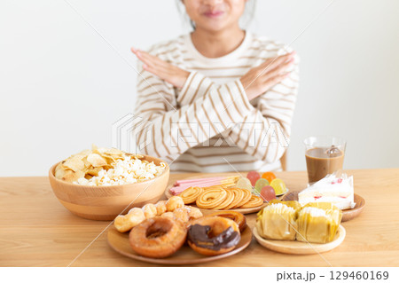 たくさんのお菓子を見てバツサインをする中学生の女の子 129460169