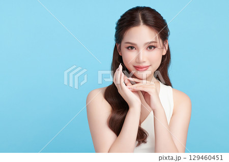 A beautiful young Asian woman with clean, fresh skin against a blue background. Skincare, facial treatment, cosmetology, beauty, and spa. An elegant portrait of an Asian woman. A beautiful young Asian woman with clean, fresh skin against a blue background. Skincare, facial treatment, cosmetology, beauty, and spa. An elegant portrait of an Asian woman. 129460451
