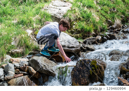 man collecting fresh mountain water from stream in the Austrian Alps 129460994