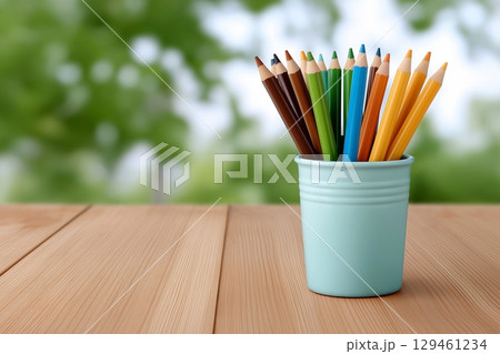 Colorful pencils in a blue cup on a wooden table, with a blurred green background. 129461234