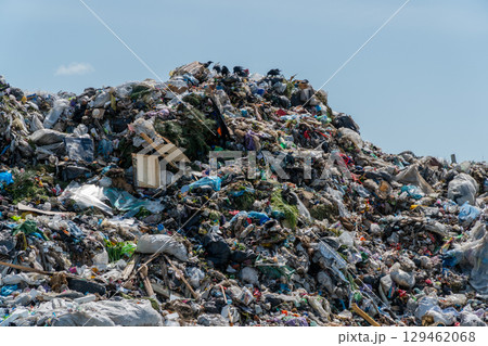 A large pile of mixed waste fills the landscape with trash, including plastics and debris, as birds circle above in a sunny urban setting A large pile of mixed waste fills the landscape with trash, including plastics and debris, as birds circle above in a sunny urban setting 129462068