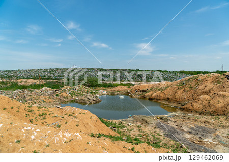 A landfill site shows heaps of waste surrounding a small body of water on a clear day, highlighting environmental concerns and pollution 129462069