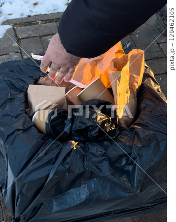 Someone is throwing away litter, including coffee cups and paper bags, into a black trash bag on a cold afternoon Someone is throwing away litter, including coffee cups and paper bags, into a black trash bag on a cold afternoon 129462105