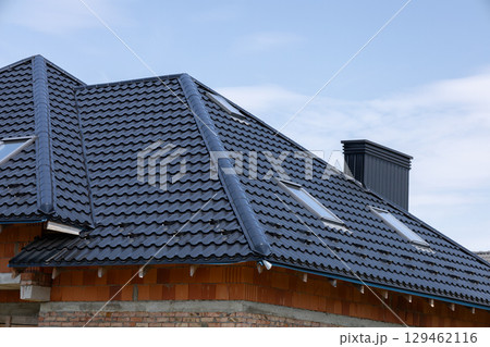 A modern home features a newly installed black tile roof with skylights under a bright blue sky, showcasing elegant design and craftsmanship 129462116