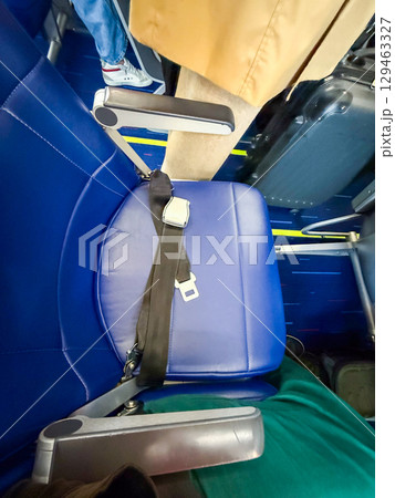 Airplane seat with fastened seatbelt and visible passengers nearby. Travel routine, onboard safety, and close-up of passenger experience. Airplane seat with fastened seatbelt and visible passengers nearby. Travel routine, onboard safety, and close-up of passenger experience. 129463327