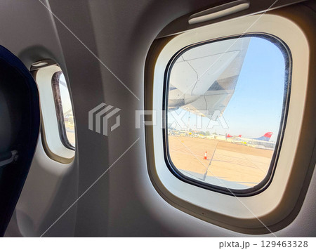 View through airplane window showing engine and runway during boarding. Travel experience, perspective, and anticipation before takeoff. 129463328