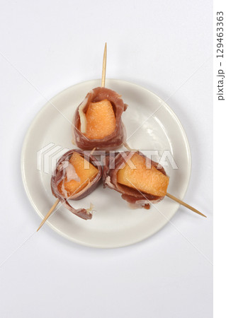 Cubes of melon wrapped in prosciutto 129463363