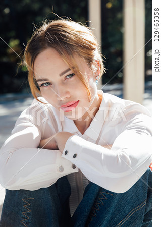 Beautiful woman in jeans and shirt sitting on the floor with a smile Beautiful woman in jeans and shirt sitting on the floor with a smile 129465358