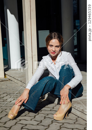 Beautiful woman in jeans and shirt sitting on the floor with a smile Beautiful woman in jeans and shirt sitting on the floor with a smile 129465359