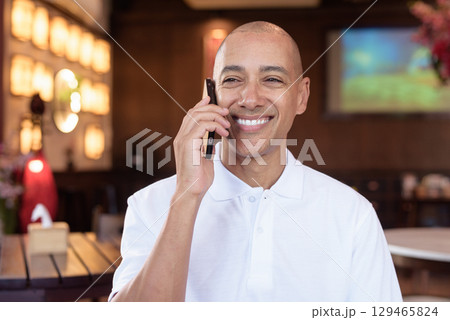 Confident Bald Hispanic man in white polo shirt sitting in Chinese style coffee shop using phone Confident Bald Hispanic man in white polo shirt sitting in Chinese style coffee shop using phone 129465824