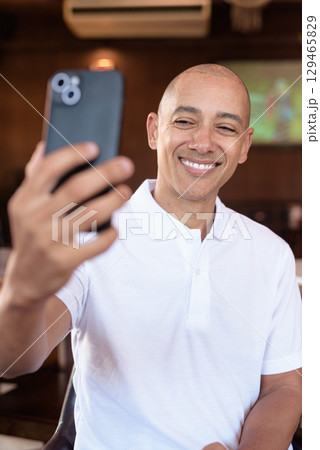 Confident Bald Hispanic man in white polo shirt sitting in Chinese style coffee shop using phone Confident Bald Hispanic man in white polo shirt sitting in Chinese style coffee shop using phone 129465829