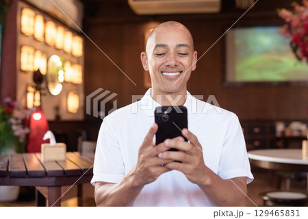 Confident Bald Hispanic man in white polo shirt sitting in Chinese style coffee shop using phone Confident Bald Hispanic man in white polo shirt sitting in Chinese style coffee shop using phone 129465831