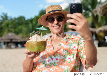 Hispanic man tourist sitting and using phone while having coconut water drink 129465943
