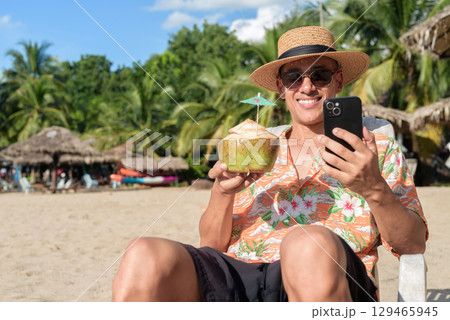 Hispanic man tourist sitting and using phone while having coconut water drink Hispanic man tourist sitting and using phone while having coconut water drink 129465945