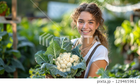 Smiling young woman holding fresh cauliflower in vegetable garden 129465961