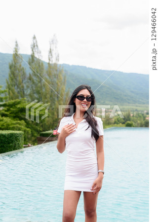 Asian woman in white polo shirt near swimming pool, outdoor nature, summer holiday portrait 129466042