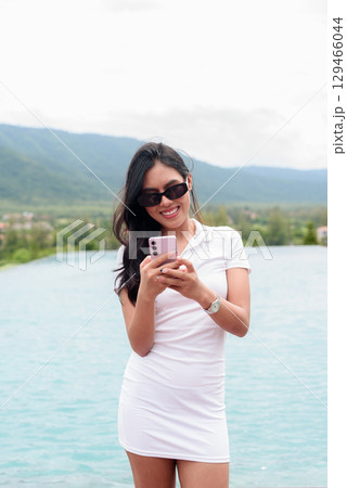 Asian woman in white polo shirt near swimming pool, outdoor nature, summer holiday portrait 129466044