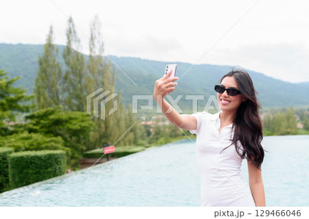 Asian woman in white polo shirt near swimming pool, outdoor nature, summer holiday portrait 129466046