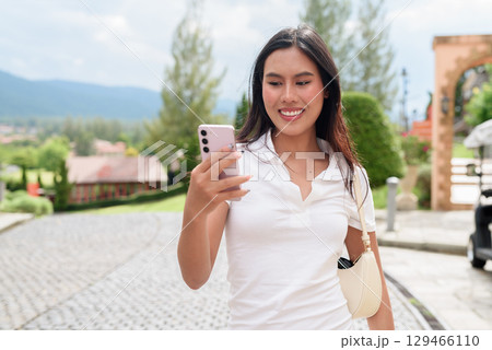 Asian woman using phone in white polo shirt on European style city street during summer 129466110