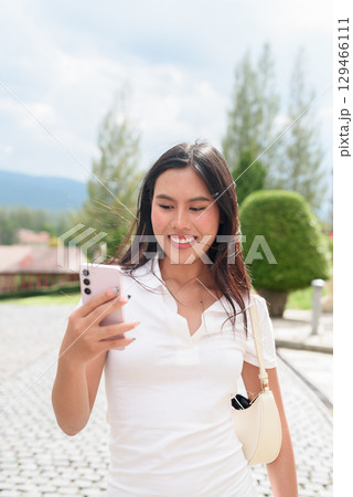 Asian woman using phone in white polo shirt on European style city street during summer 129466111