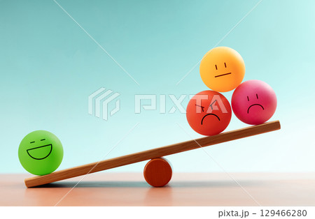 Colorful emotional faces balancing on a seesaw, symbolizing mental health and emotional self-regulation through balancing positive and negative emotions 129466280