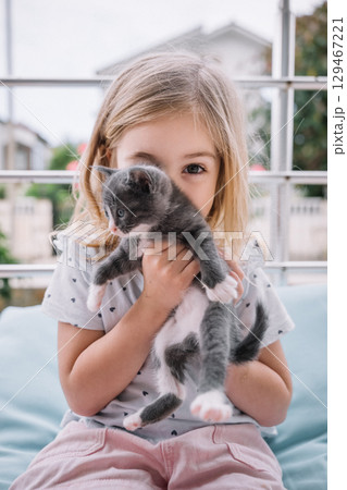 Little girl joyfully holding a gray kitten at home during a sunny afternoon 129467221