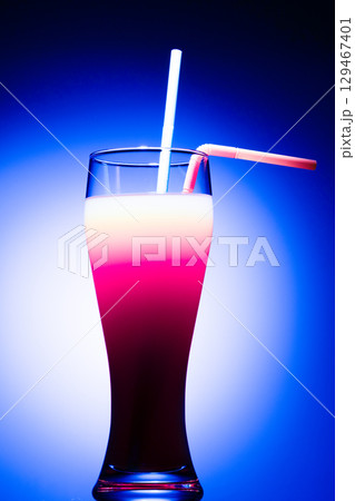 A layered cocktail in a tall glass, featuring distinct white, pink, and dark red purple layers, illuminated against a  129467401