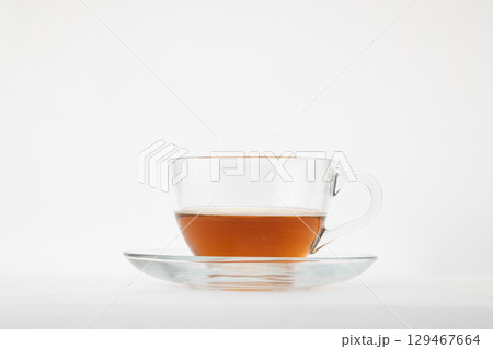 A clear glass teacup filled with amber-colored tea, possibly black or rooibos, resting on a matching clear glass saucer A clear glass teacup filled with amber-colored tea, possibly black or rooibos, resting on a matching clear glass saucer 129467664