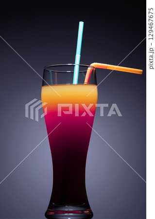 Two straws are inserted into the glass: one is light blue and straight, while the other is orange and bent 129467675