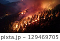Forest wildfire raging through mountainous terrain at night, illuminating the trees with flames and smoke 129469705