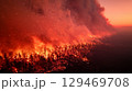 Wildfire raging through forest landscape at sunset, with flames illuminating trees and smoke billowing into the sky 129469708