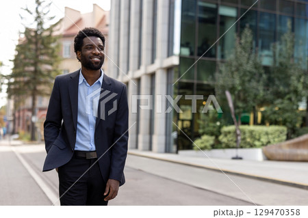 A professional man in formal clothing walking outside a contemporary building, exuding confidence and positivity. The modern cityscape and green surroundings create a dynamic and fresh atmosphere. A professional man in formal clothing walking outside a contemporary building, exuding confidence and positivity. The modern cityscape and green surroundings create a dynamic and fresh atmosphere. 129470358
