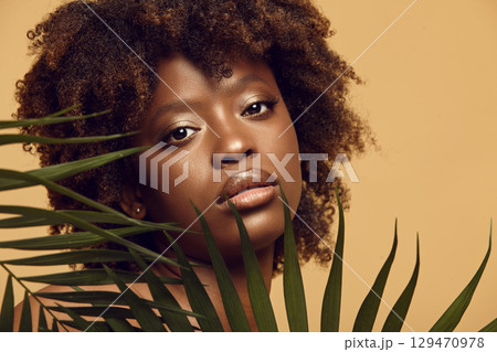 Sexy black girl watching intently from behind palm leaves. Sexy black girl watching intently from behind palm leaves. 129470978