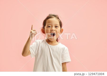 Joyfully Excited Asian Child Girl Sharing with Finger to Up Symbolizing Arose of Genius Idea or Just Points up at Empty Space Above Her Expression Happy Surprised Standing On Pink Isolated Background 129471004
