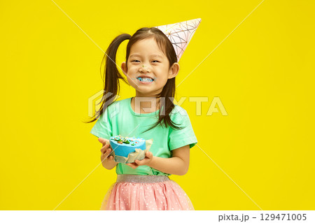 Joyful Child Girl Dressed in Party Clothes Enjoying Birthday Cake and Cheerful Smiling Over Yellow Isolated Joyful Child Girl Dressed in Party Clothes Enjoying Birthday Cake and Cheerful Smiling Over Yellow Isolated 129471005