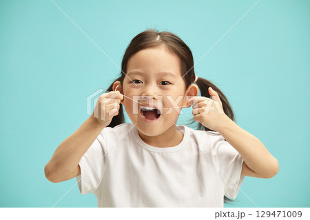 Female japanese child with mouthly wide open clean myself her teeth with a dental floss, close up isolated portrait. Five years old asian ethnicity girl using oral hygiene staff. Female japanese child with mouthly wide open clean myself her teeth with a dental floss, close up isolated portrait. Five years old asian ethnicity girl using oral hygiene staff. 129471009