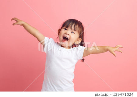 Joyful little Asian girl with her arms outstretched expresses fun and pleasure on isolated pink background. Happy child concept. Joyful little Asian girl with her arms outstretched expresses fun and pleasure on isolated pink background. Happy child concept. 129471024