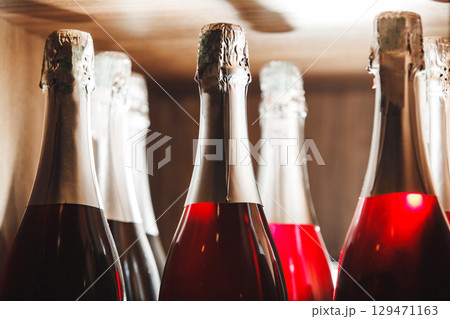 Close-Up of Sparkling Rose Wine Bottles on Wooden Shelf in Ambient Light 129471163