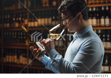 Professional Wine Expert Evaluating Quality and Checking Bottle Label in Cellar 129471171
