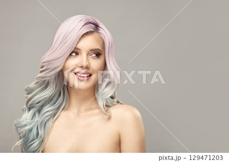 Cheerful woman with long curly pink and blue color hair looks aside on beige background. Cheerful woman with long curly pink and blue color hair looks aside on beige background. 129471203