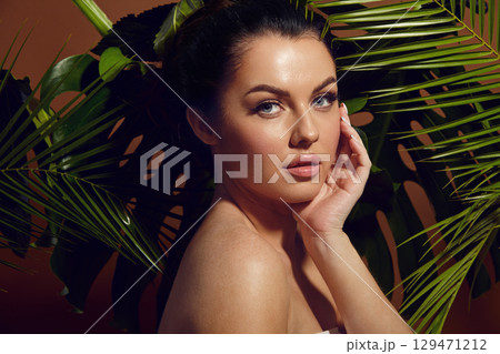 Young woman on a tropical leaves background, beauty studio portrait. 129471212