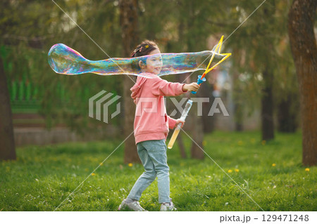 Happy Girl Blows Large Bubble in Park on Sunny Day 129471248